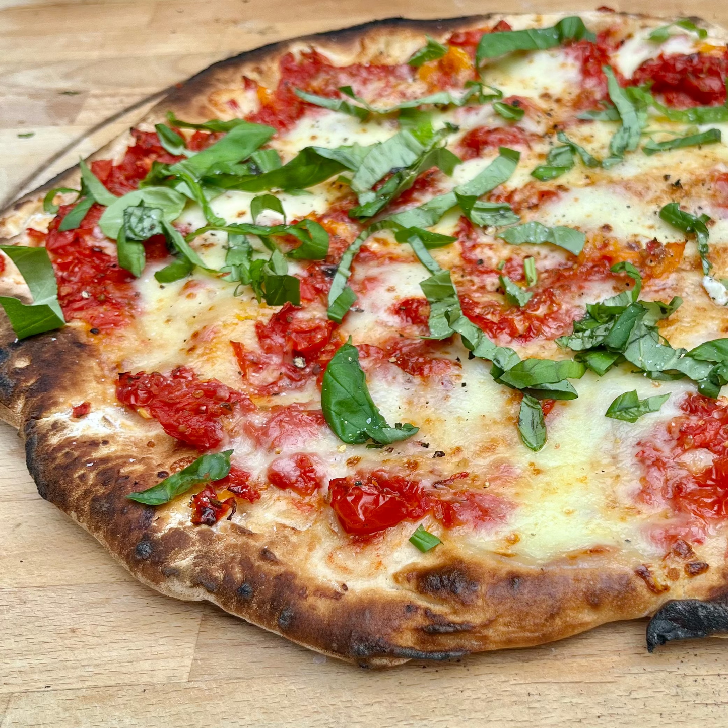 Pizza with tomato sauce, cheese, and basil on a wooden surface